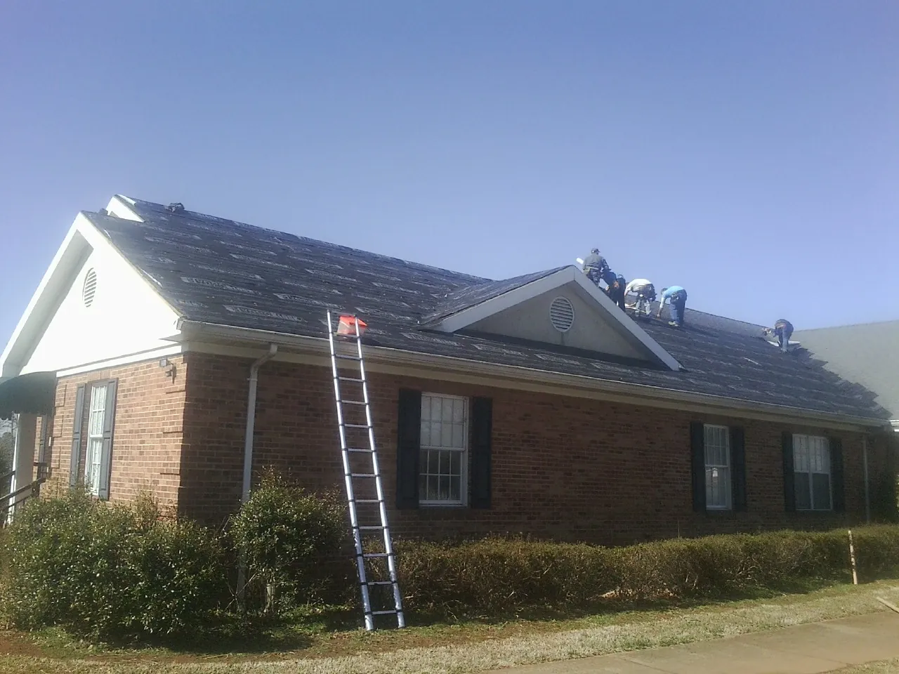 Crew tearing shingles off a brick ranch roof with a ladder set — Emergency Roof Repair work by our crew in Orangevale