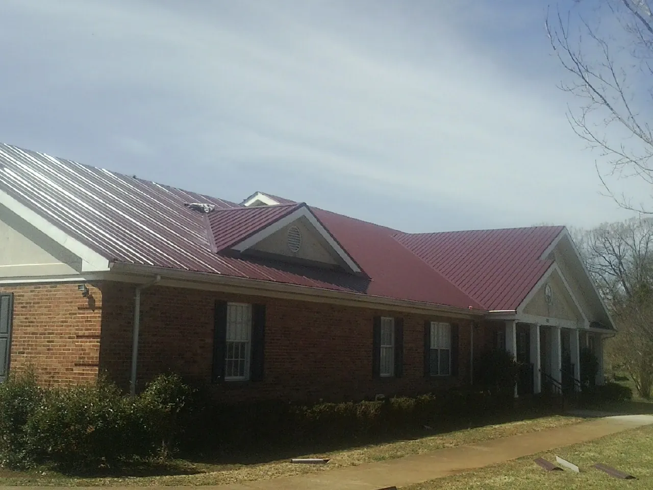 Red metal roof with gabled entries on a long brick building, from a Hail Damage Roof Repair job in Orangevale
