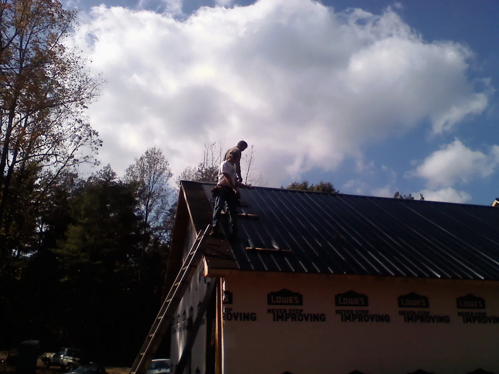 Roofer fastening dark metal panels high against a cloudy sky, from a Roof Inspection job in Orangevale